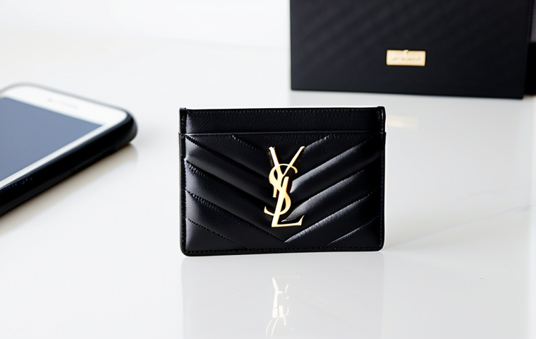 A minimalist Saint Laurent Monogram cardholder crafted from black quilted leather, adorned with a subtle gold YSL logo. The sleek cardholder is positioned on a clean, modern white desk next to a contemporary smartphone. The background is a soft-focus, bright, professional office environment with ample natural light. Captured with precise product photography, studio quality, sharp focus, high detail, perfect anatomy, correct proportions. Safe for work, appropriate content, fully clothed, professional, modest.